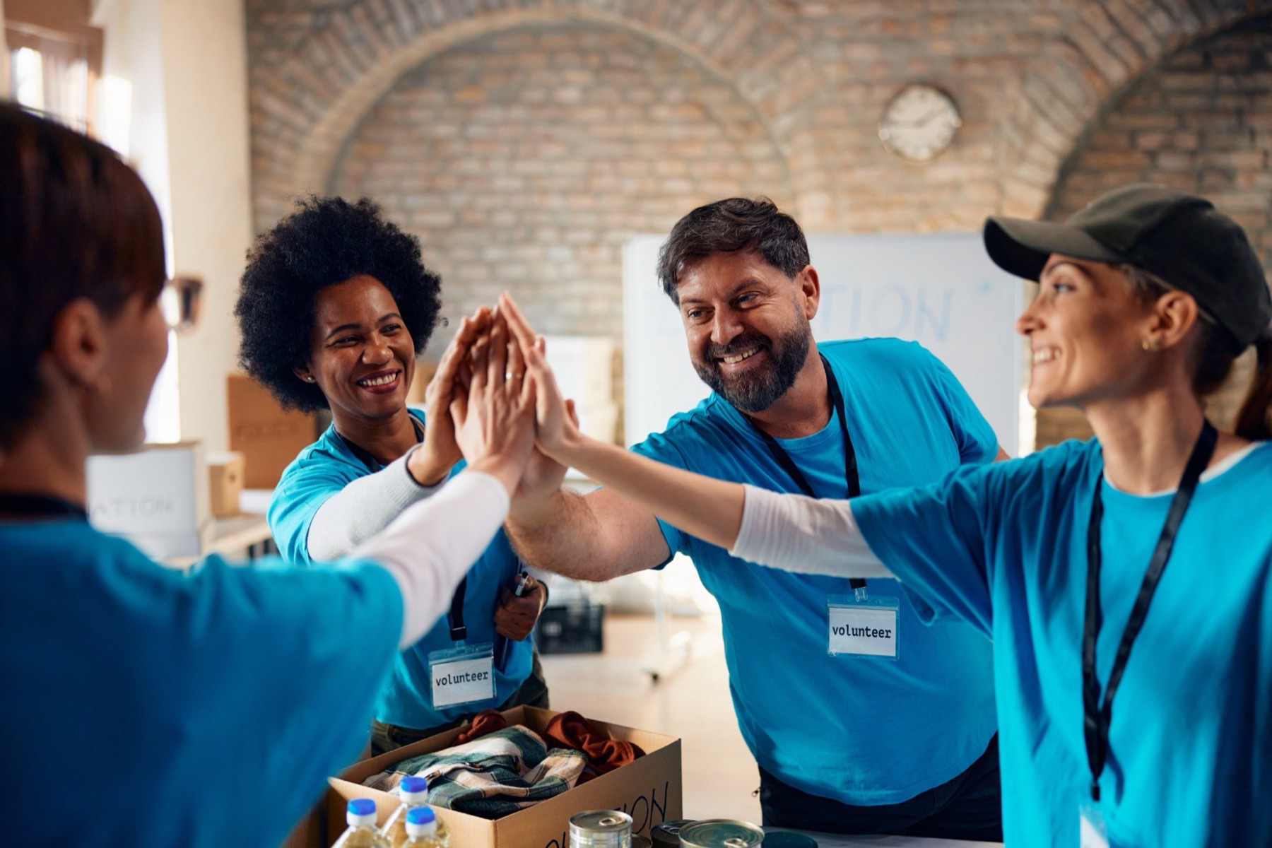 Equipe de voluntários de camiseta azul e crachá batendo as mãos juntas em cima de uma mesa de doações